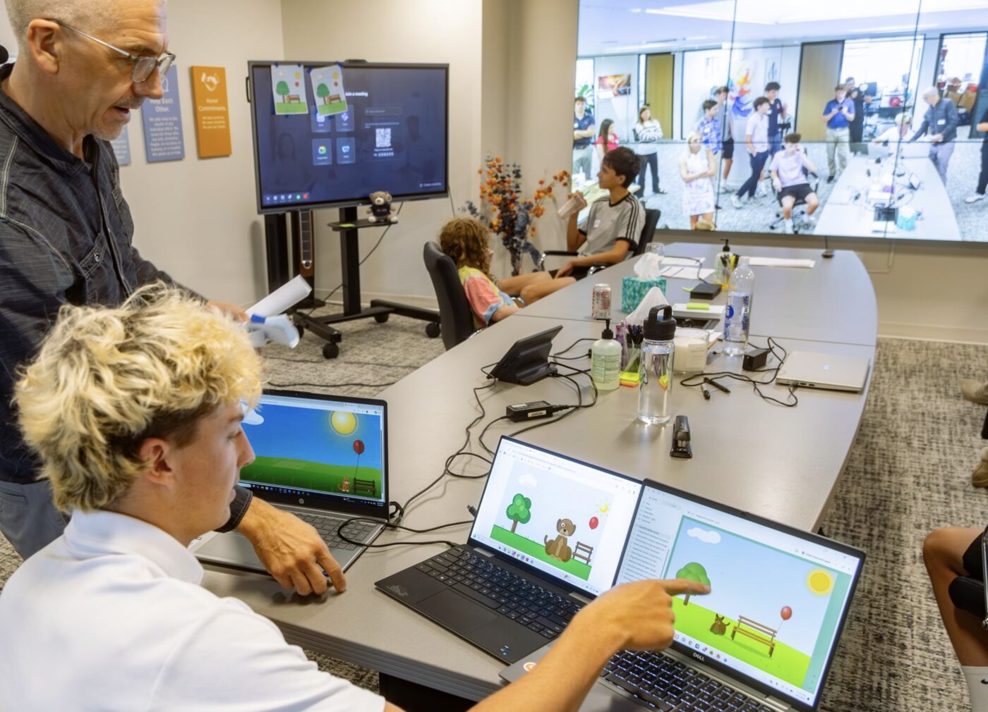 Participants show their AI-built scenes on laptops while a PhoenixTeam practitioner looks on